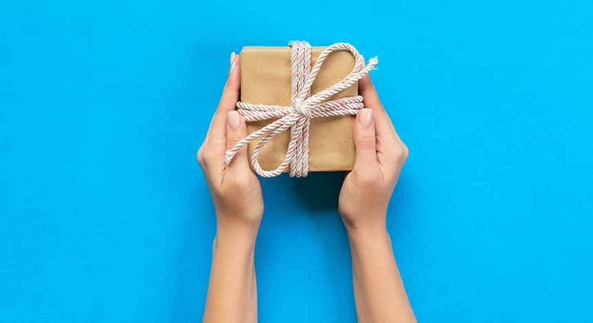 Woman hands holding gift wrapped present in paper with ribbon.  The gift is in front of a blue background