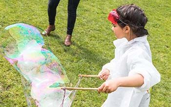 A girl in a mad science lab coat making a bubble using 2 sticks and a rope