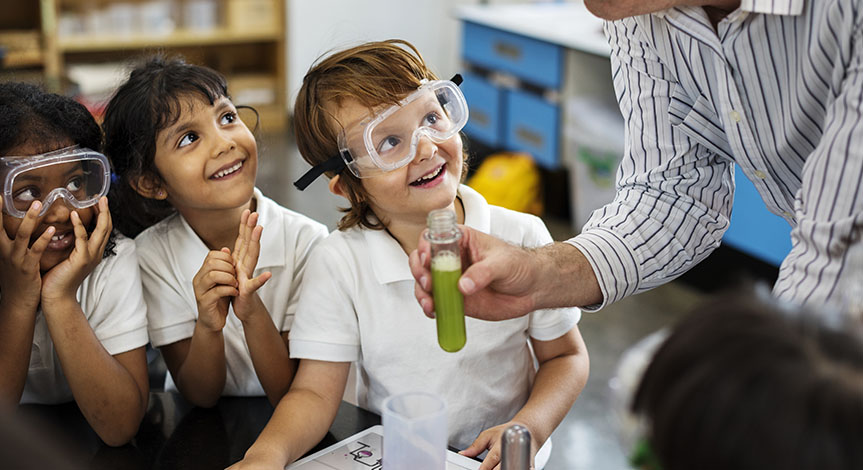 4 kids looking at teacher while he holds a test tube with a green substance inside