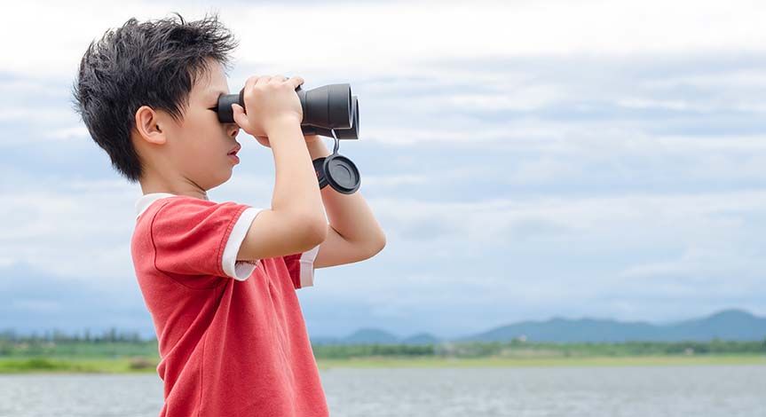 Boy in a field looking through binoculars