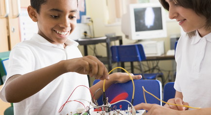 Boy and girl playing with wires attached to circuit board on a desk